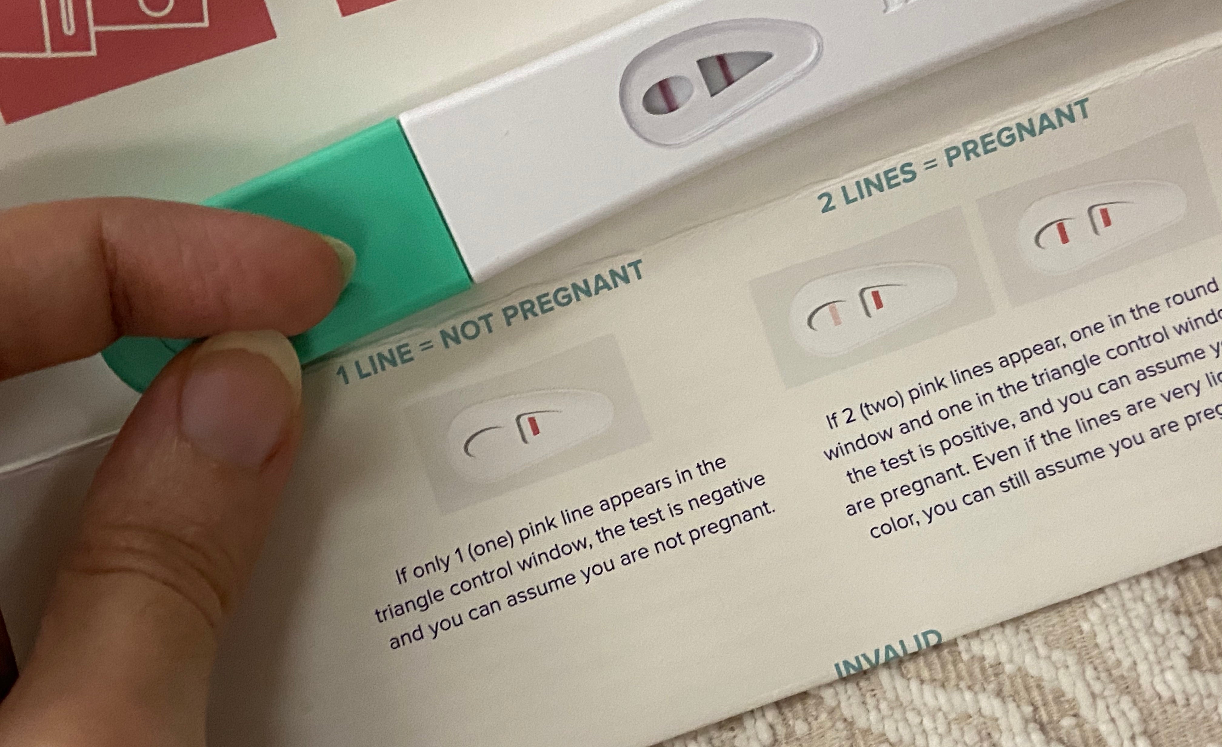 Hand with long nails holds a positive Mosie Baby Pregnancy Test above the instructions.