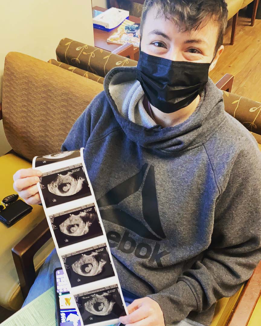 Mama to be wearing black medical mask smiles and shares sonogram images announcing Mosie Baby!