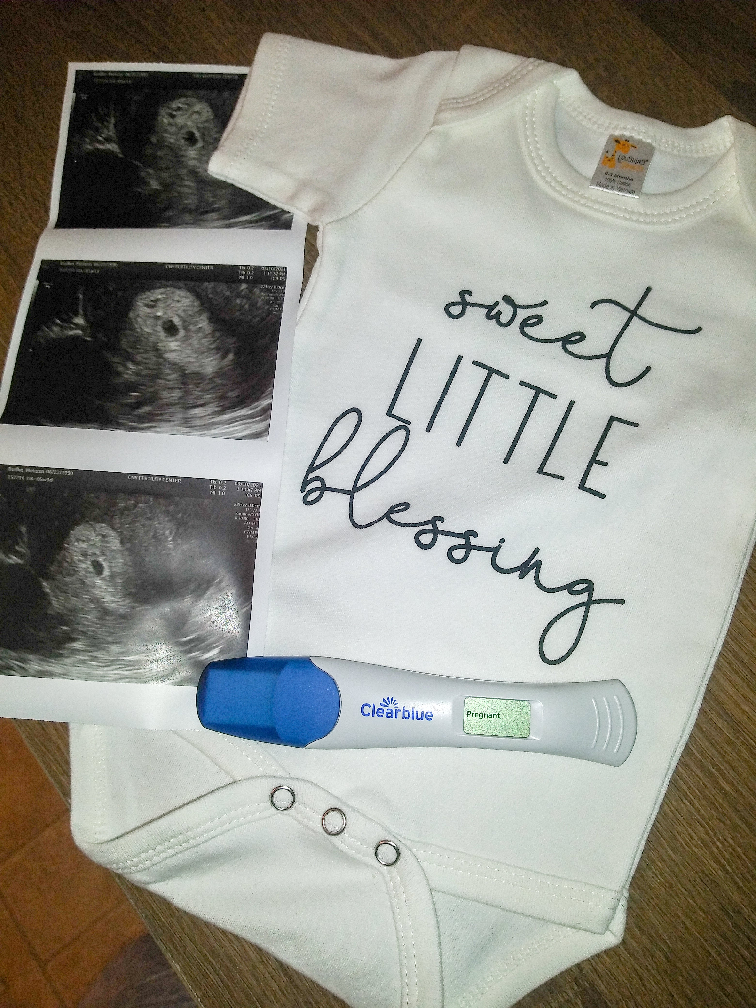 Flat lay of three sonogram photos on the left, white onesie on the right with text that reads: sweet little something. And a positive pregnancy test on the bottom.