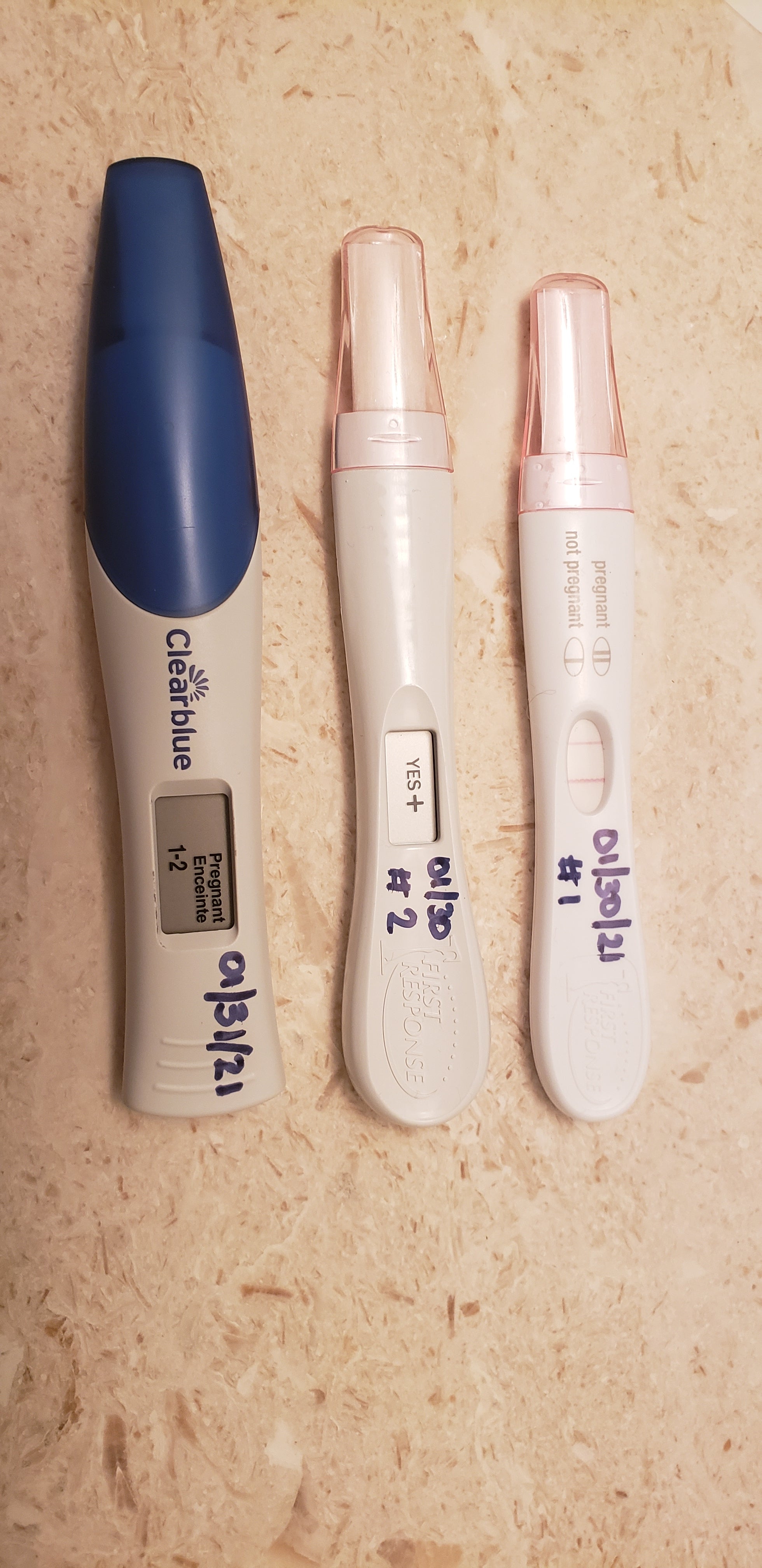 Three positive pregnancy tests vertically laid over a marble counter.