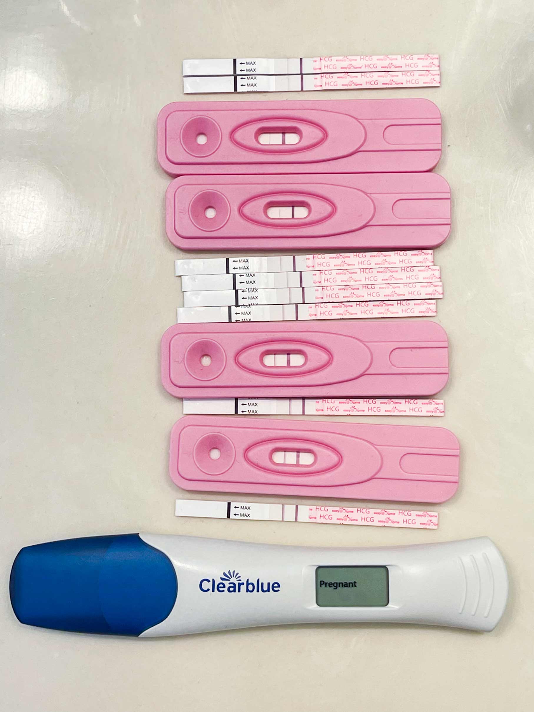 Several positive strip pregnancy tests and one clear blue test lined up vertically announcing Mosie Baby!