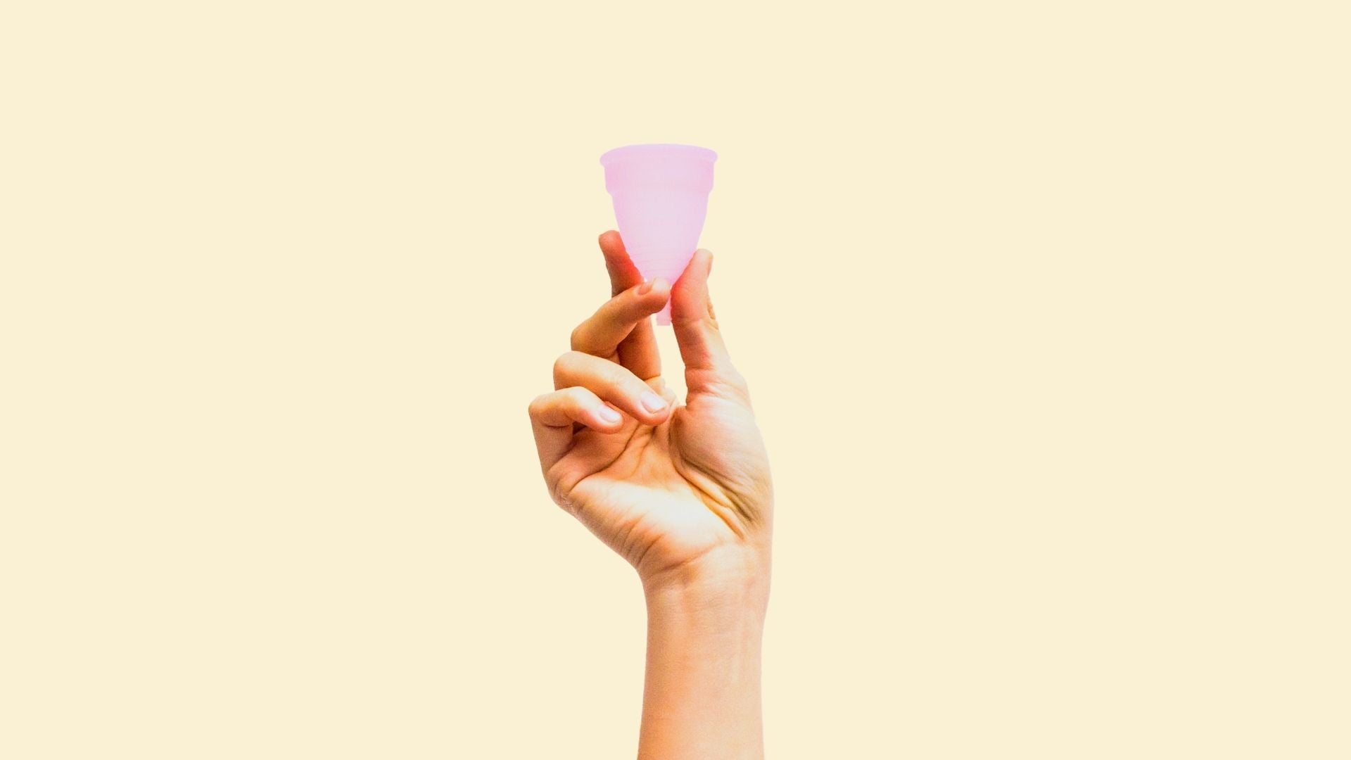 Woman's hand holding up pink soft menstrual cup over beige background