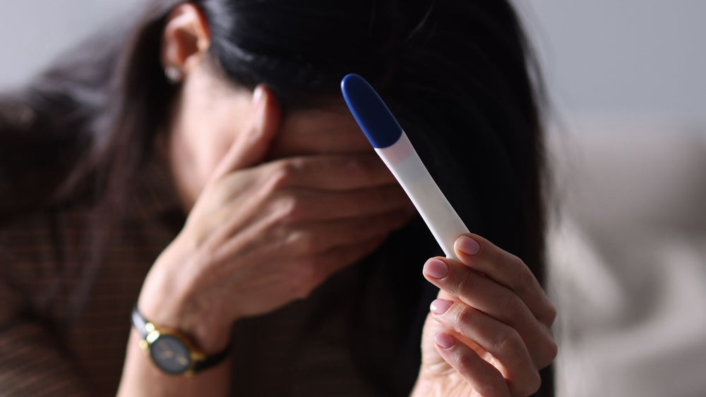 Women covers face with hand in grief while holding pregnancy test