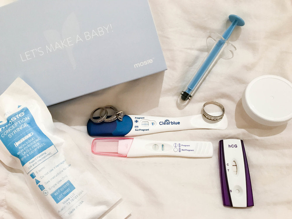 three positive pregnancy tests with the mosie baby box, syringe, and their wedding rings