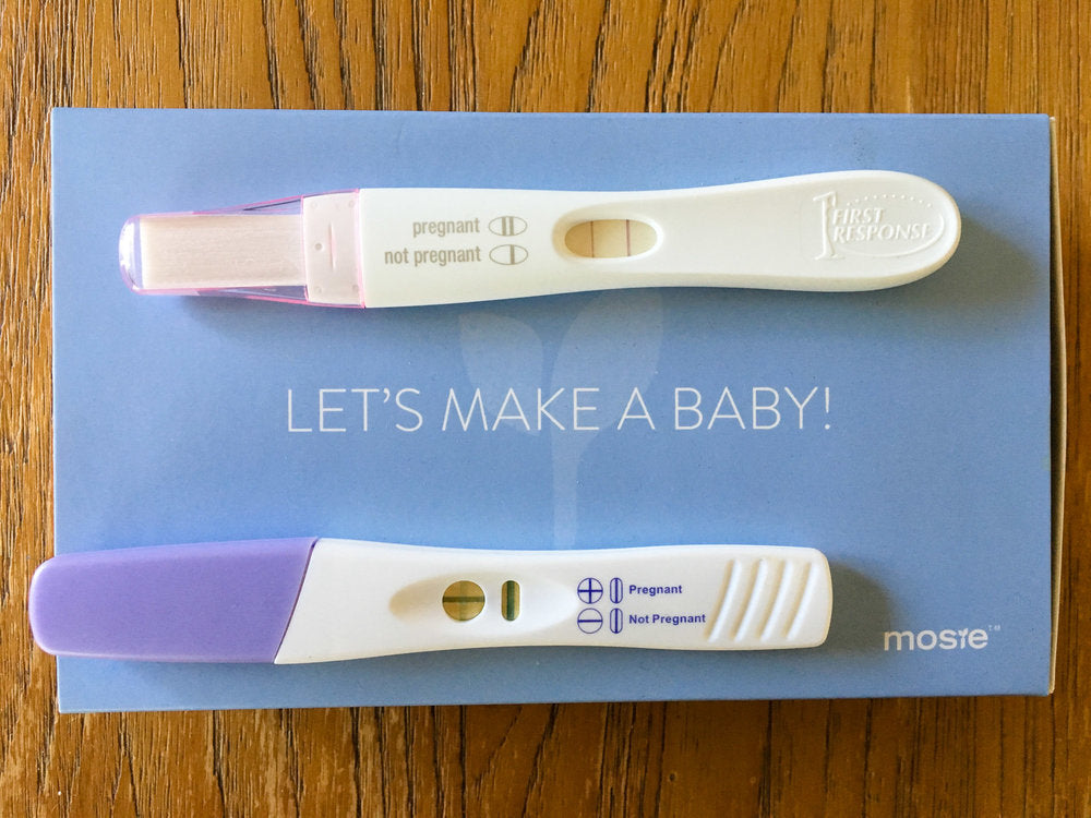 Two positive pregnancy tests on top of a Mosie Baby box