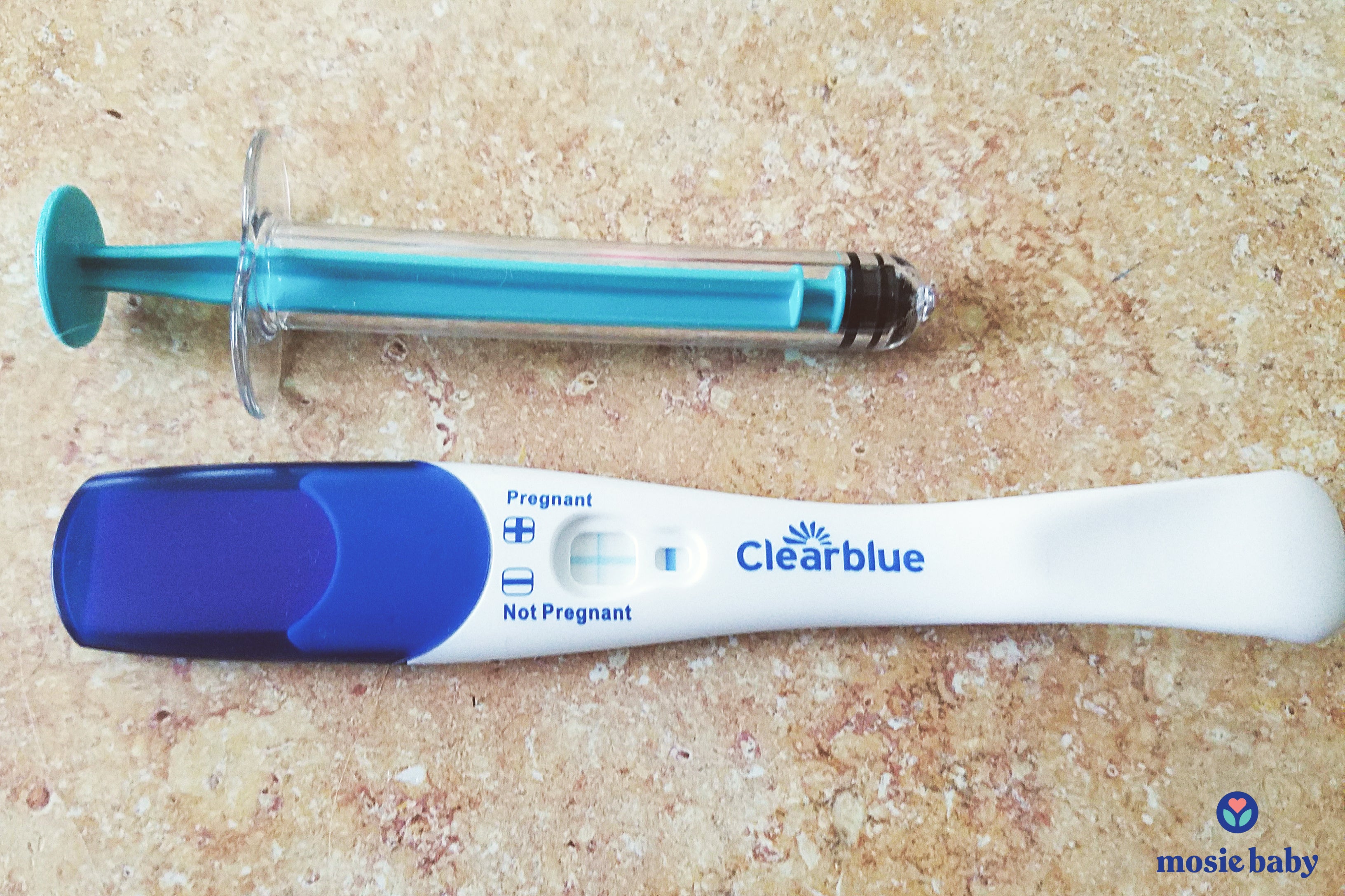 positive pregnancy test next to a mosie baby syringe