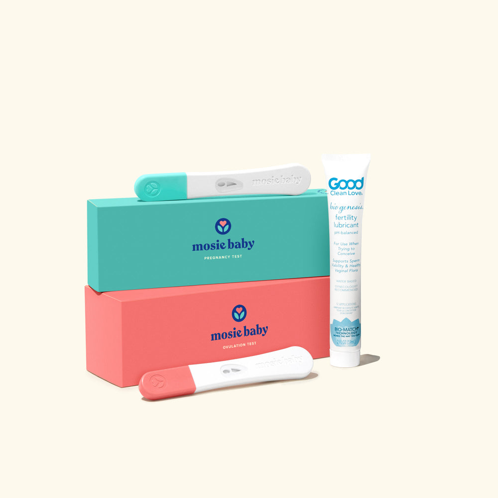 The teal rectangular ovulation test box with an oulation test on top is stacked on top of the pink rectangular pregnancy test box. A pregnancy test is in front of it. xBiogenesis™ Good Clean Love Fertility Lubricant stands next to it, against a beige background